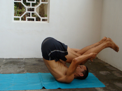 rolling back 3, rolling on the back with spine rounded as a preparation for plow pose and shoulder stand and as an ab exercise. In this picture I've rolled up onto my shoulders and am balanced with my center of gravity over my shoulders. Hips are high and legs are reaching back to help get my center of gravity over my shoulders. Neil Keleher. Sensational Yoga Poses.