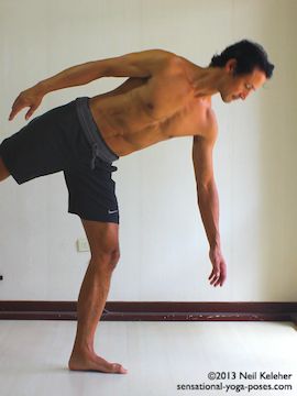 Balancing on one foot while moving into half moon yoga pose (ardha chandrasana. Standing with the foot turned out, turn the pelvis to the front and slowly reach to the floor while lifting the free leg. This picture shows the the mid point position with weight on one leg pelvis facing the front and bottom arm reaching towards the floor. Torso is nearly horizontal. Neil Keleher. Sensational Yoga Poses.