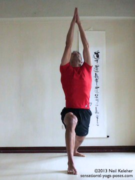, yoga standing poses, warrior (virabhadrasana) 1. In warrior 1 one knee is bent and the other is straight with both feet flat on the floor. The bent knee foot faces forwards in the same direction as the pelvis. The knee is bent 90 degrees with shin vertical. Torso reaches straight up and the arms reach up over the head with elbows straight and palms touching. Gaze in this picture is upwards so that head is tilted backwards. Feet are positioned so that the heels are on one straight line.