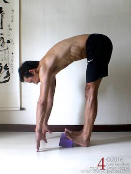 Standing calf stretch while bending forwards, fronts of feet elevated with yoga block. Hips back to reduce stretch.