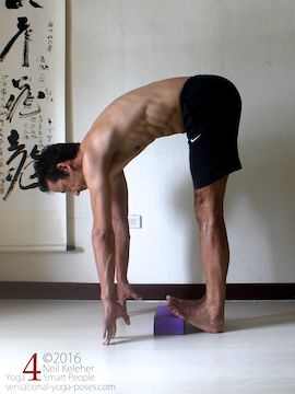 Standing calf stretch while bending forwards, fronts of feet elevated with yoga block.
